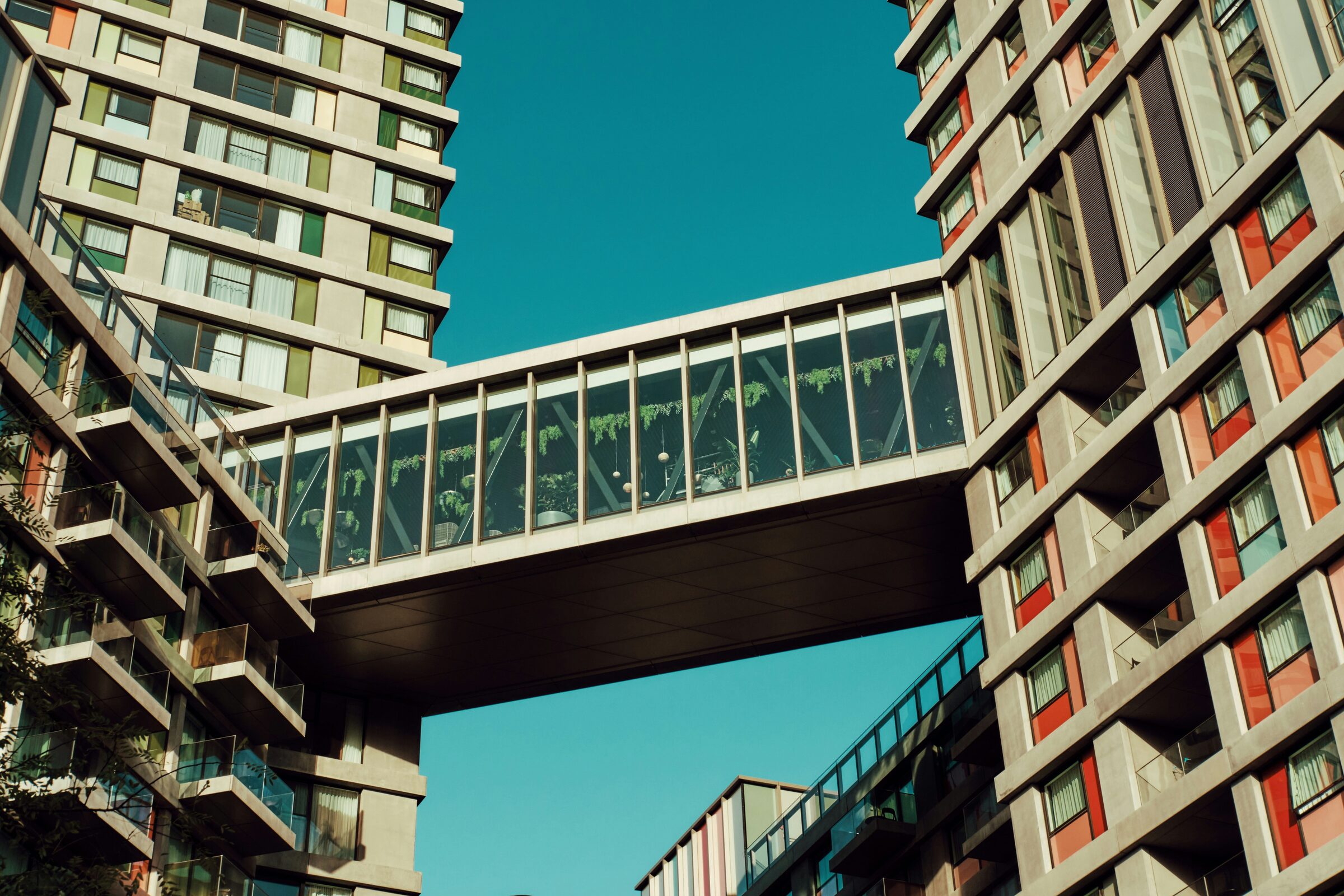 A glazed skybridge linking two apartment towers against a clear blue sky