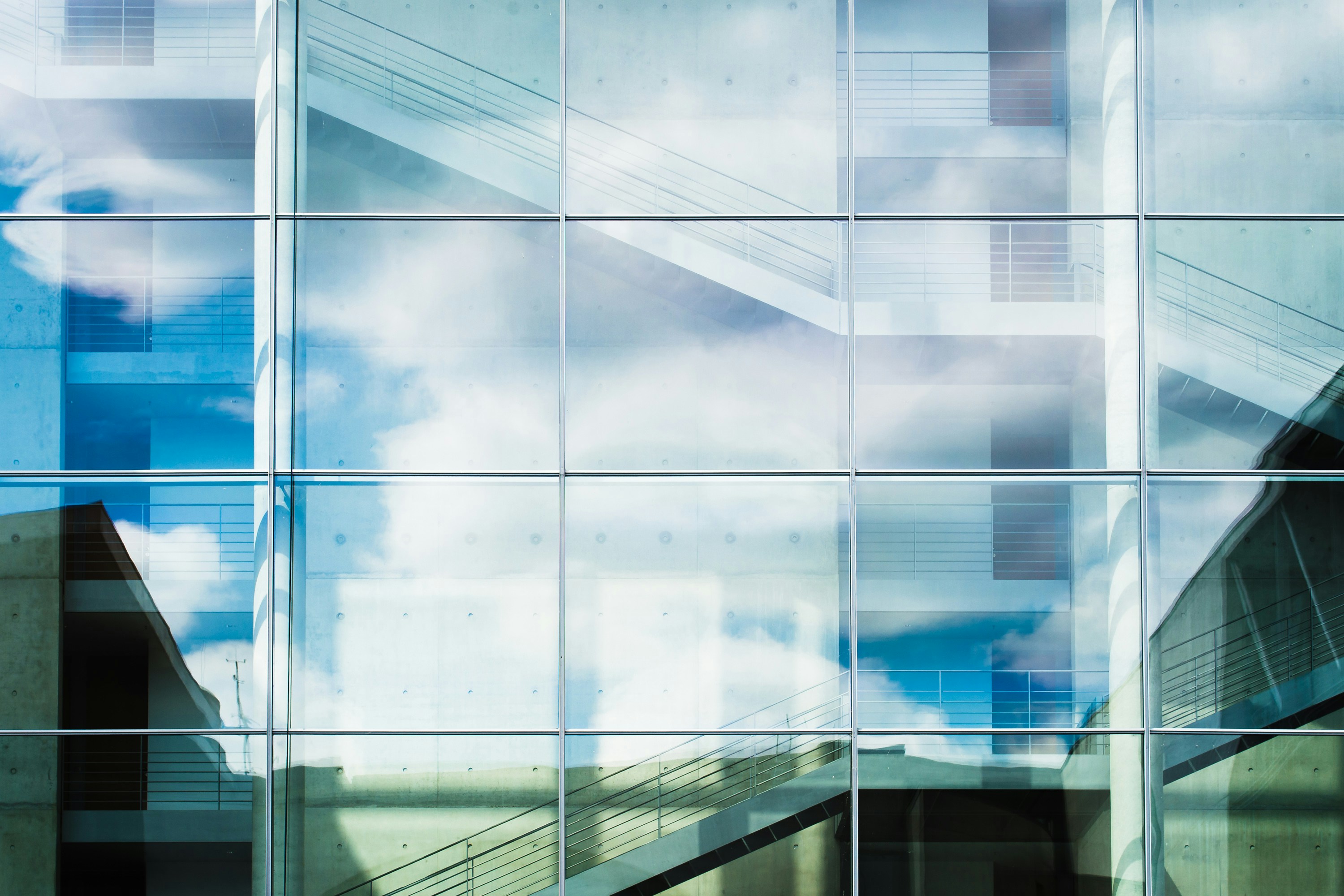 Glass facade reflecting sky, clouds and stairways